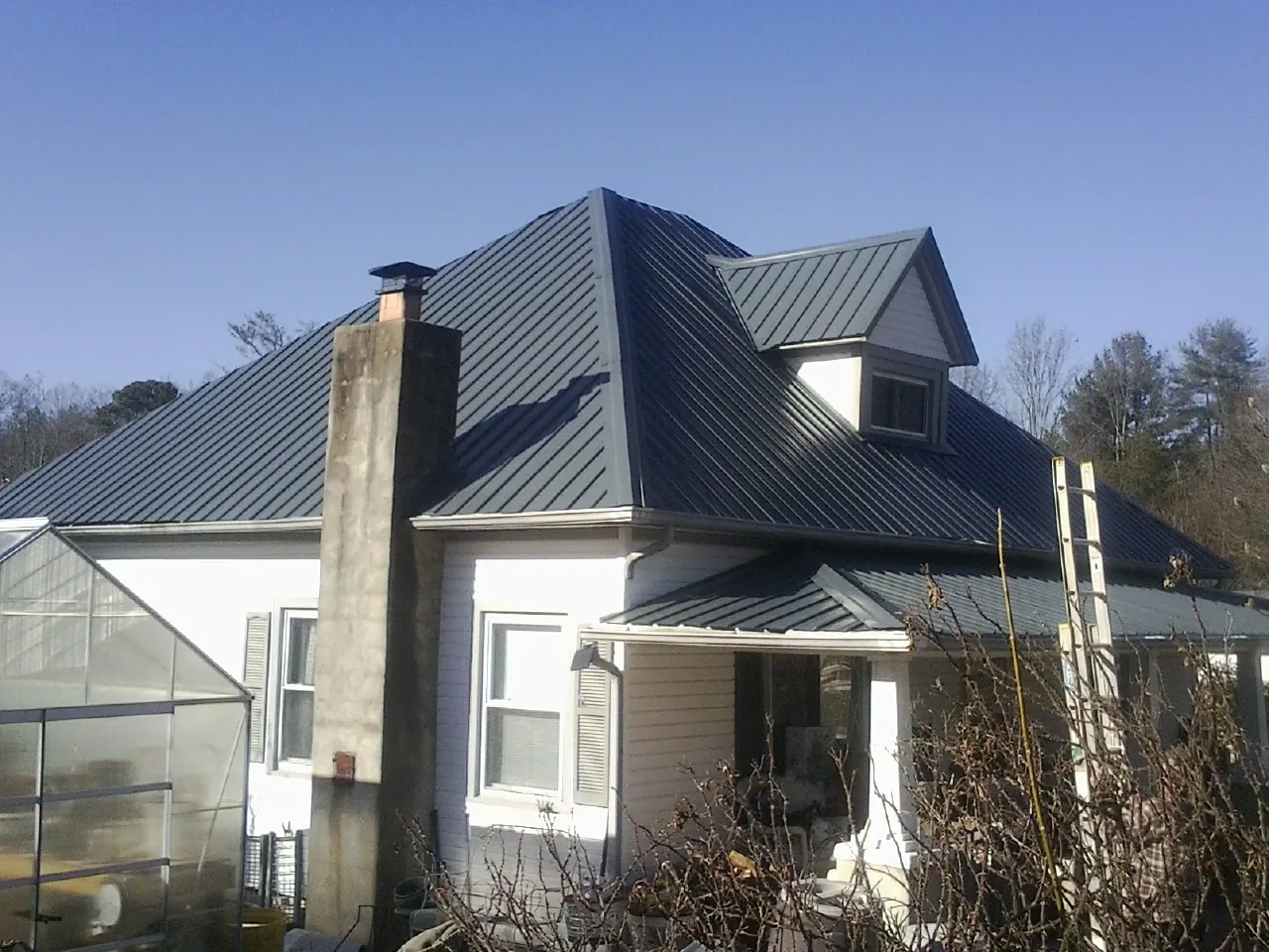 Dark blue standing seam metal roof on a white farmhouse with dormer — Slate & Tile Roof Repair by Roofing Brothers in Labelle