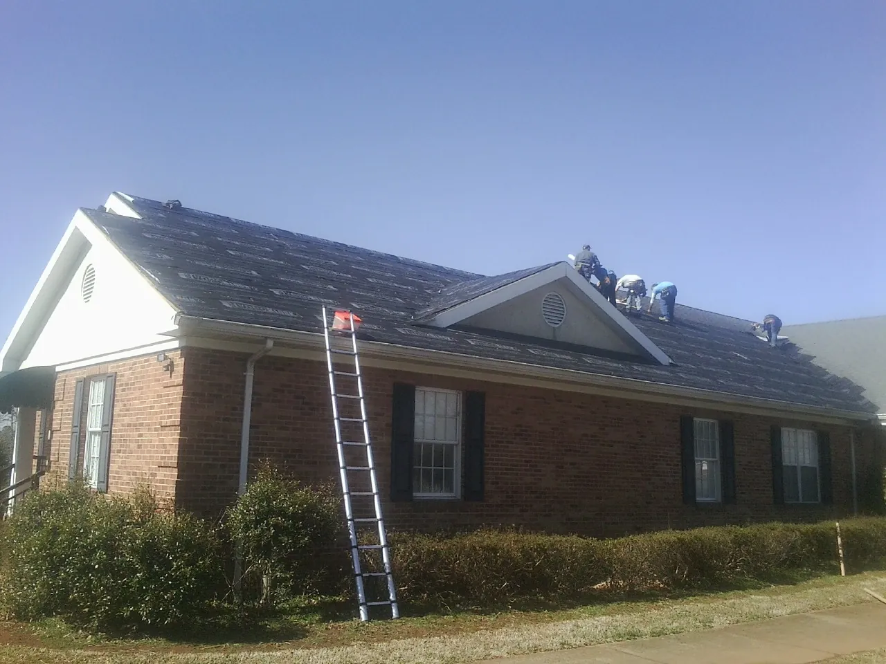 Crew tearing shingles off a brick ranch roof with a ladder set — Metal Roof Repair work by our crew in Labelle