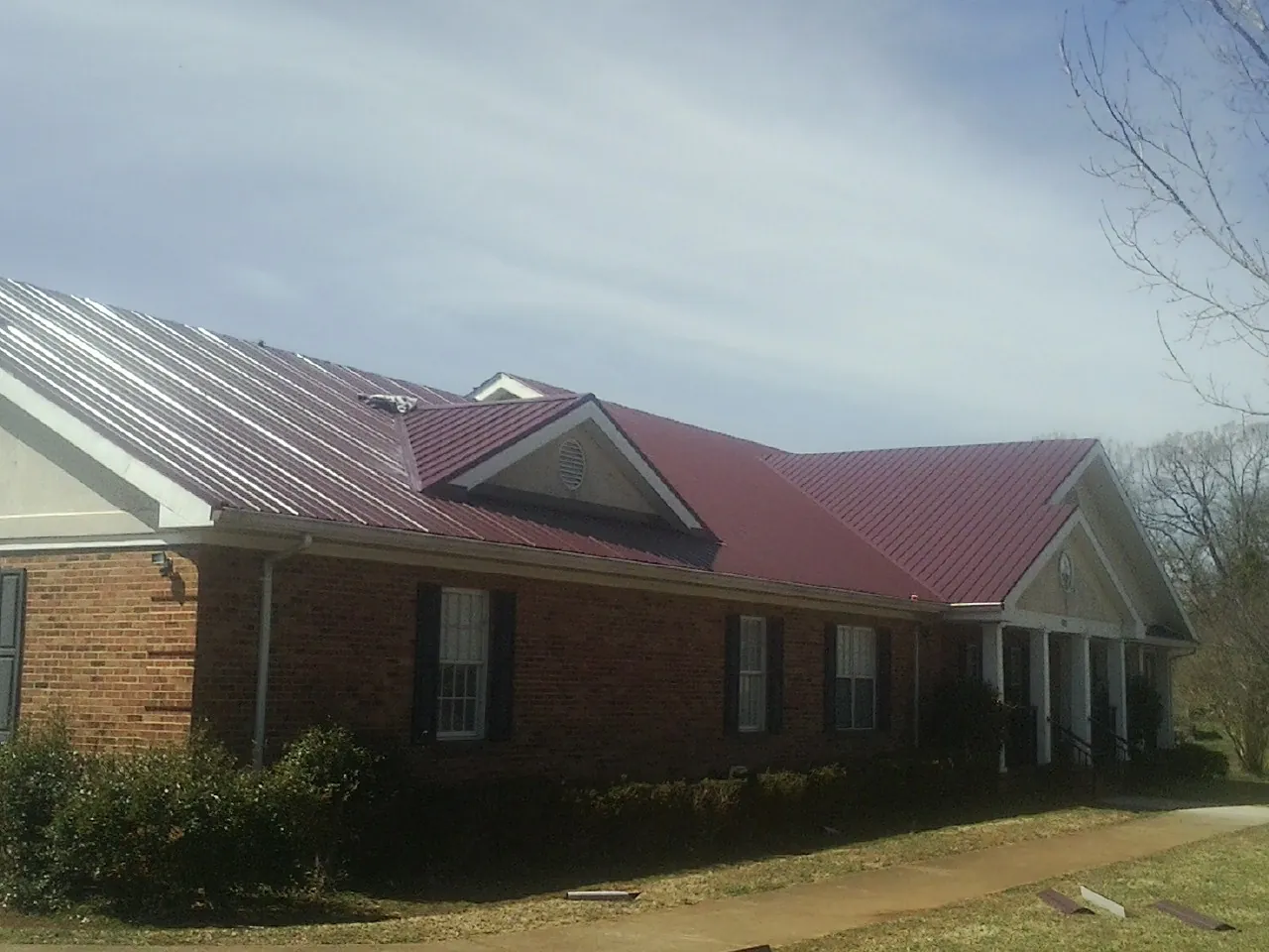 Red metal roof with gabled entries on a long brick building, from a Hail Damage Roof Repair job in Labelle
