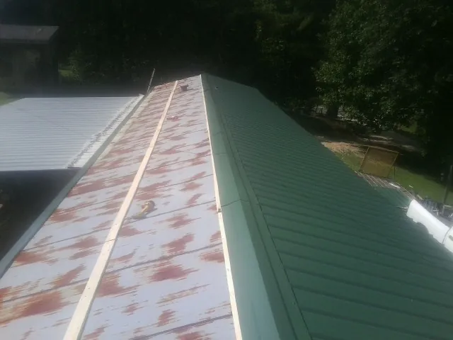 Old rusted panels beside newly installed green metal roofing — Wind Damage Roof Repair by Roofing Brothers in Labelle